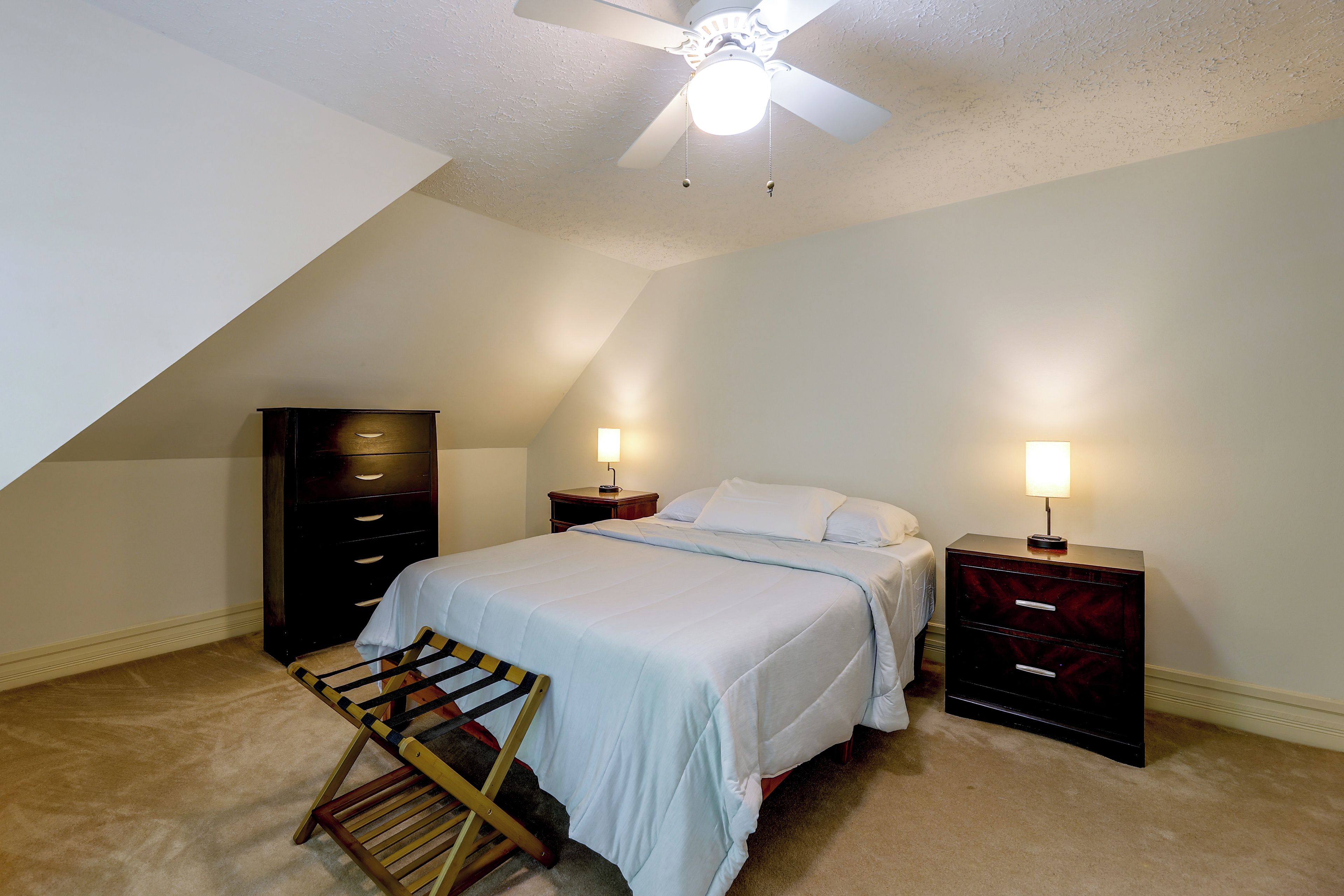A bedroom with a bed, two bedside tables with lamps, a wardrobe, and a ceiling fan.