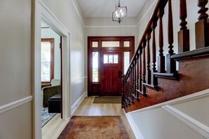 A hallway with a wooden staircase, a door with glass panels, and a light fixture. - Tuskegee 5BR Home in Historic District (Tuskegee)