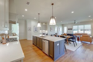 A modern kitchen with a central island, a dining area with a sofa and chairs, and a living room with a large window.