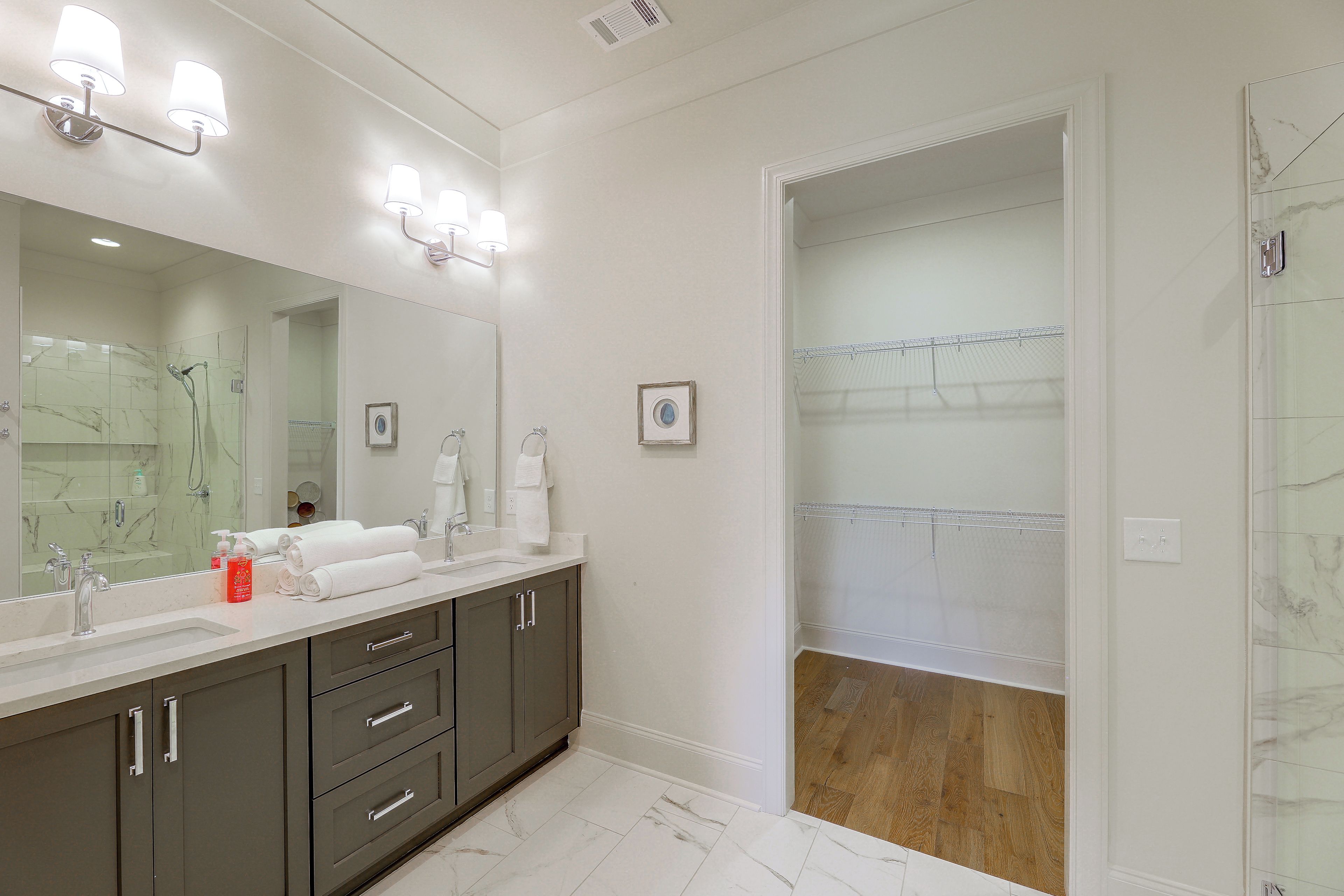 A modern bathroom with a large mirror, dual sinks, and a walk-in shower.