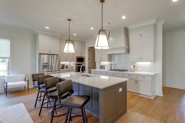 A modern kitchen with a central island, bar stools, stainless steel appliances, and pendant lighting.