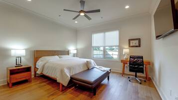 A bedroom with a bed, bedside tables, a bench, a desk with a chair, a ceiling fan, and a window with blinds.