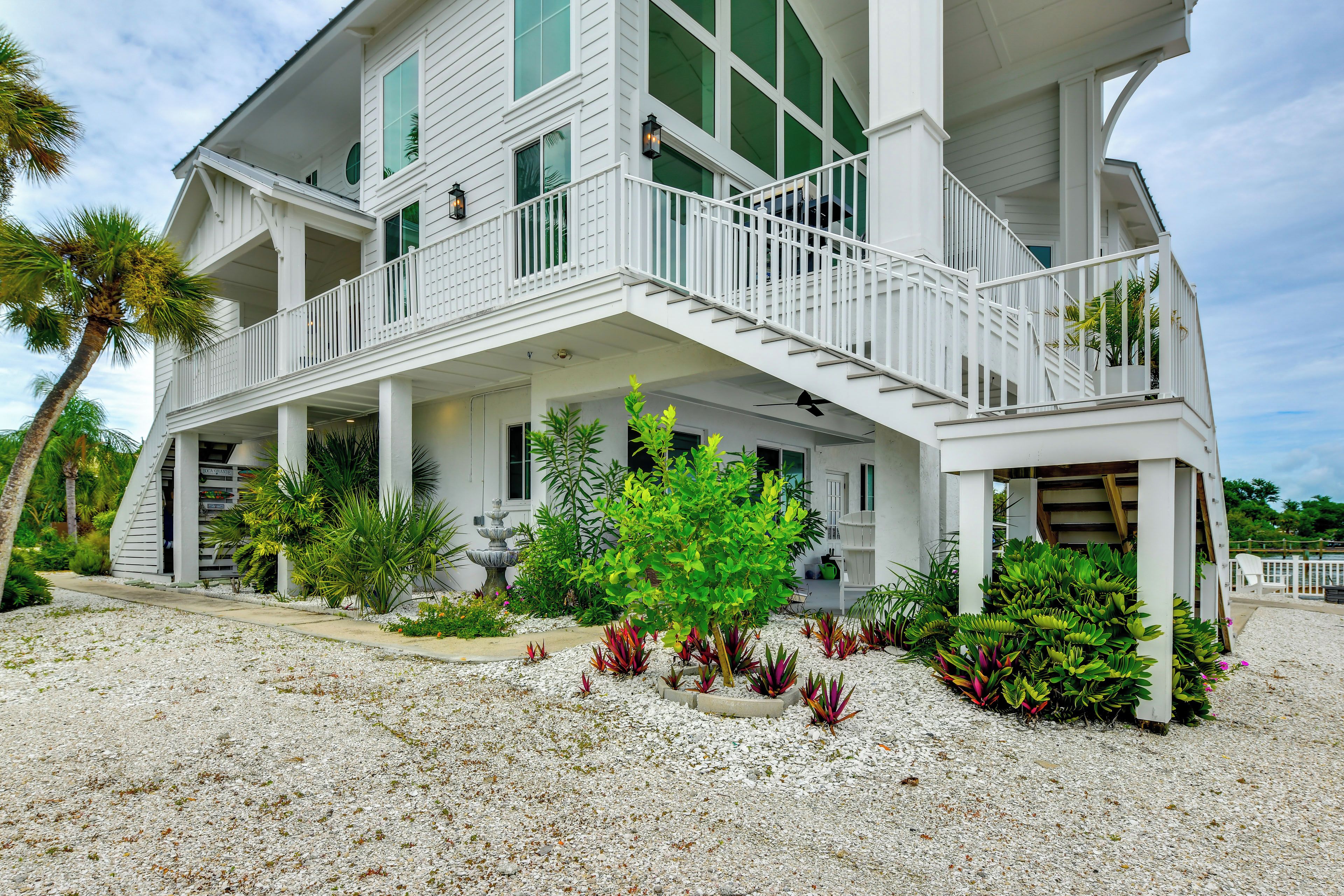 A two-story house with a balcony, a covered porch, and a garden with various plants.