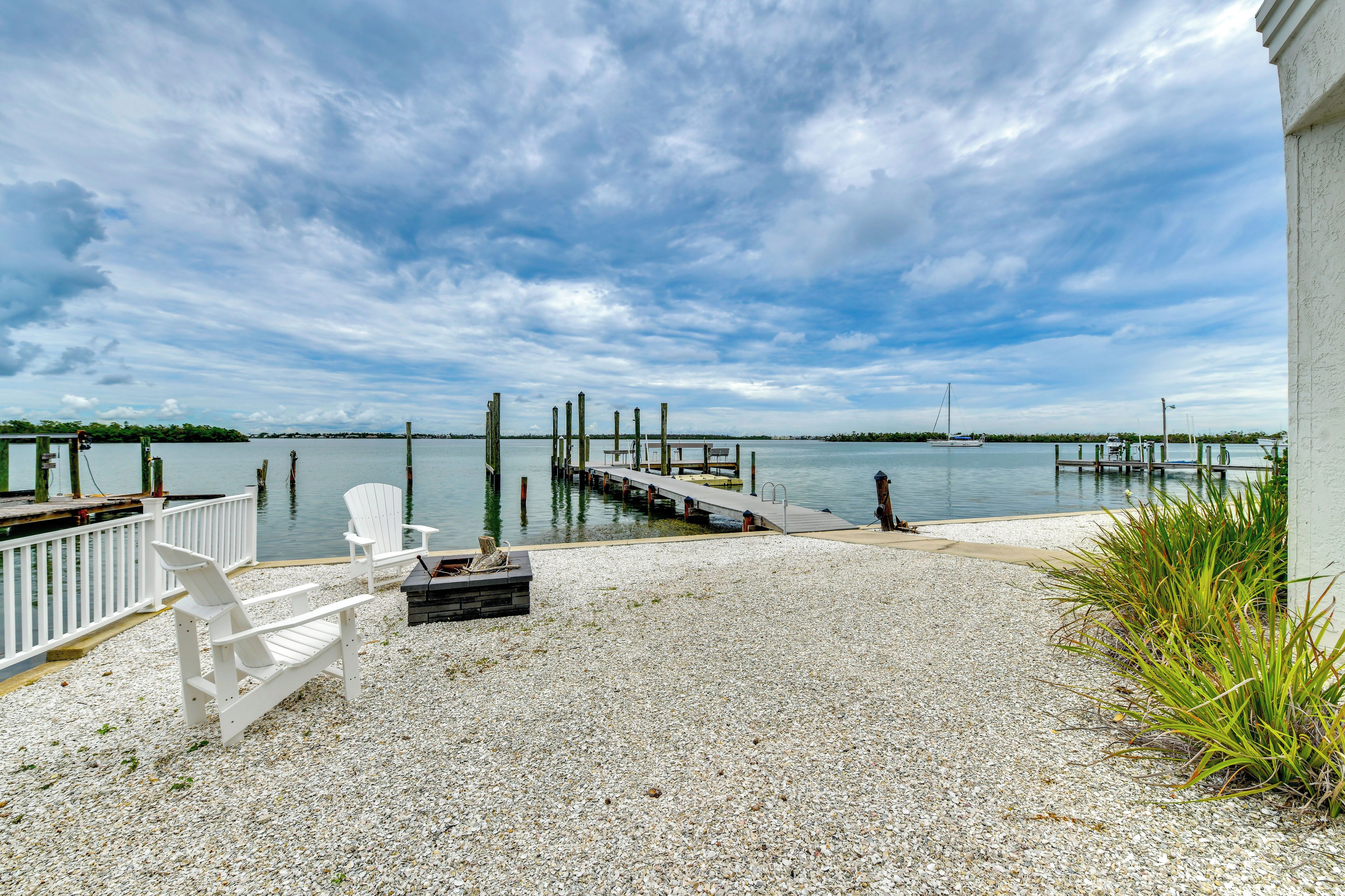 A waterfront patio with a dock, white chairs, and a gravel surface.