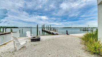 A waterfront patio with a dock, white chairs, and a gravel surface.