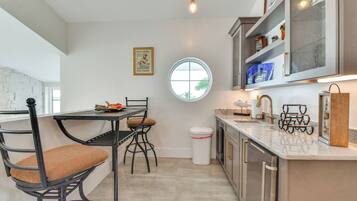 Una cocina moderna con comedor, que cuenta con un ventanal redondo, un cubo de basura y un cuadro en la pared.