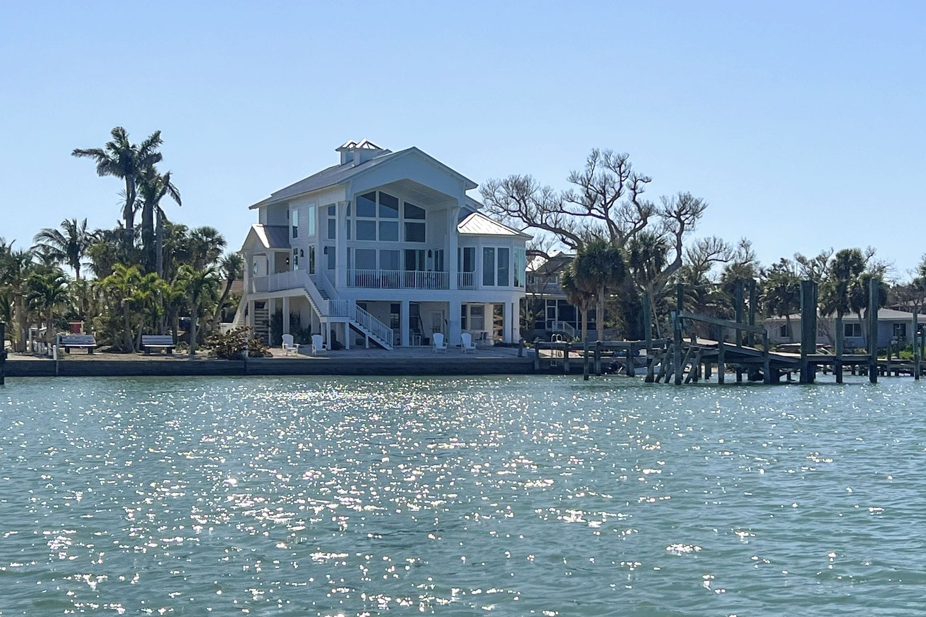A large, multi-story waterfront property with a covered deck and a dock extending into the water.
