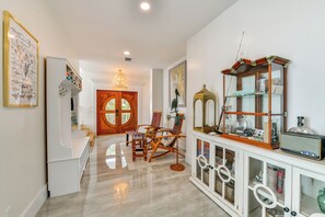 A hallway with a wooden door, a rocking chair, a glass cabinet with decorative items, and a framed shark illustration on the wall. - Luxury Bayfront Home, Private Dock, Steps to Beach (Englewood)