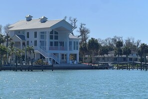 A waterfront property with a large house featuring multiple balconies, a dock, and a clear view of the water.