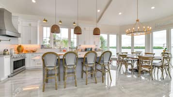 A modern kitchen with white cabinetry, a central island with bar stools, and a dining area with a large table and chairs.