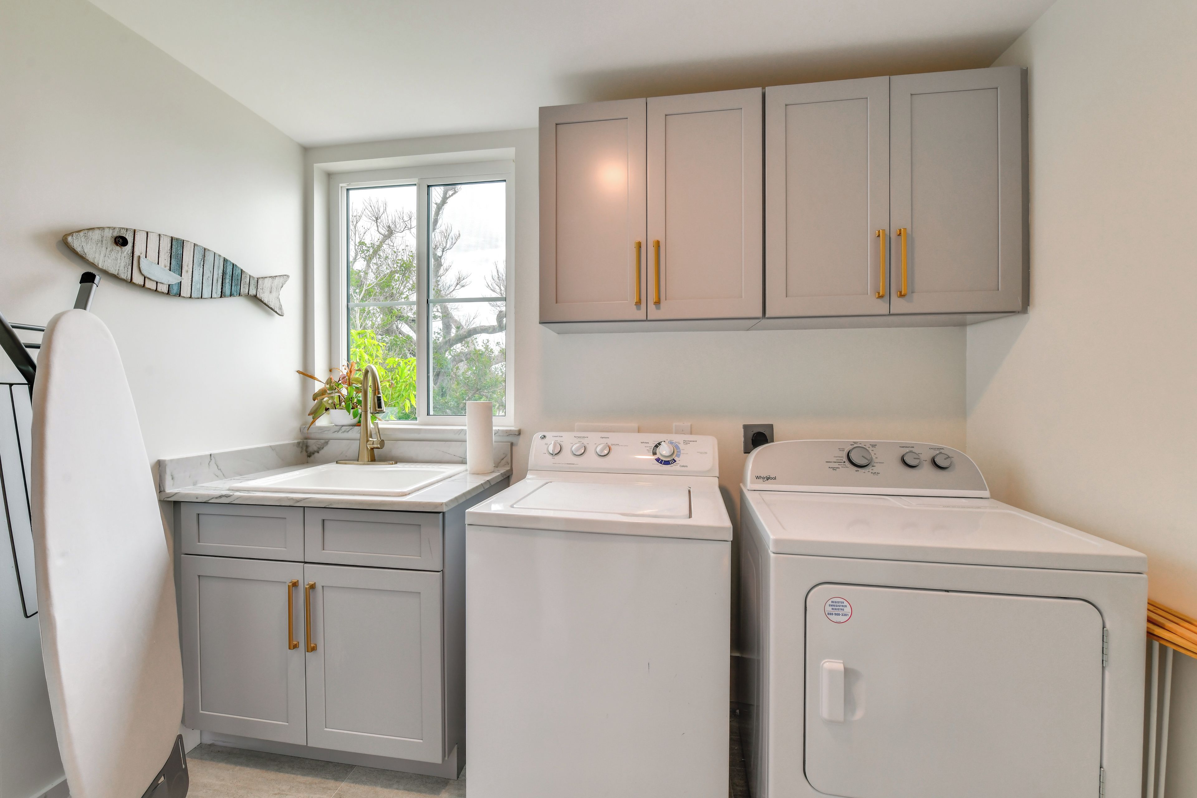 A laundry room with two washing machines, a sink, and a window with a view of trees.