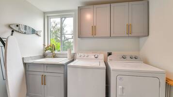 A laundry room with two washing machines, a sink, and a window with a view of trees.