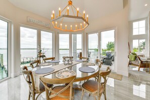 A spacious dining area with a view of the water, featuring a chandelier, round tables, and wicker chairs. - Luxury Bayfront Home, Private Dock, Steps to Beach (Englewood)