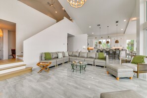 A spacious living area with a large L-shaped sectional sofa, a glass coffee table, and a dining area with a kitchen in the background.
