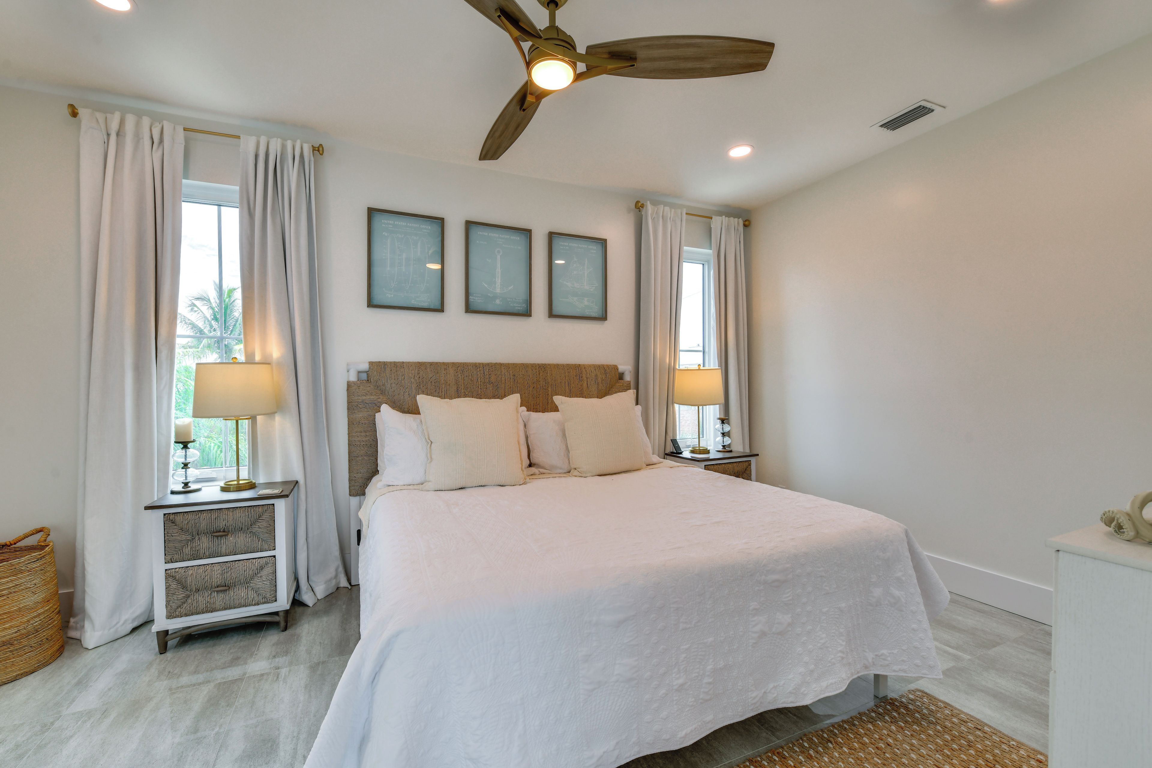 A bedroom with a large bed, two bedside tables with lamps, a ceiling fan, and three framed certificates on the wall.
