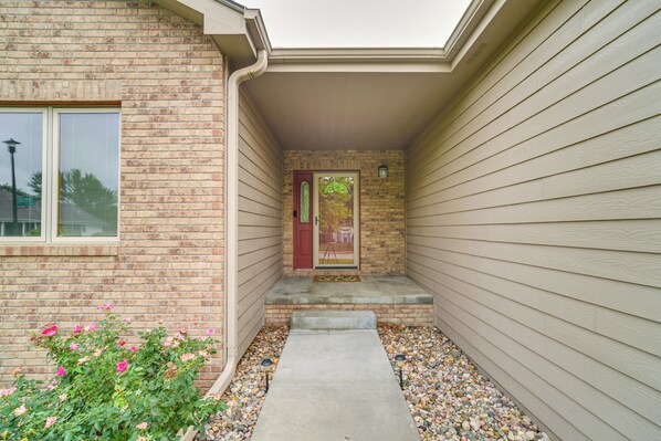 A residential building with a brick facade, a red door, and a small porch area with steps leading to the entrance.