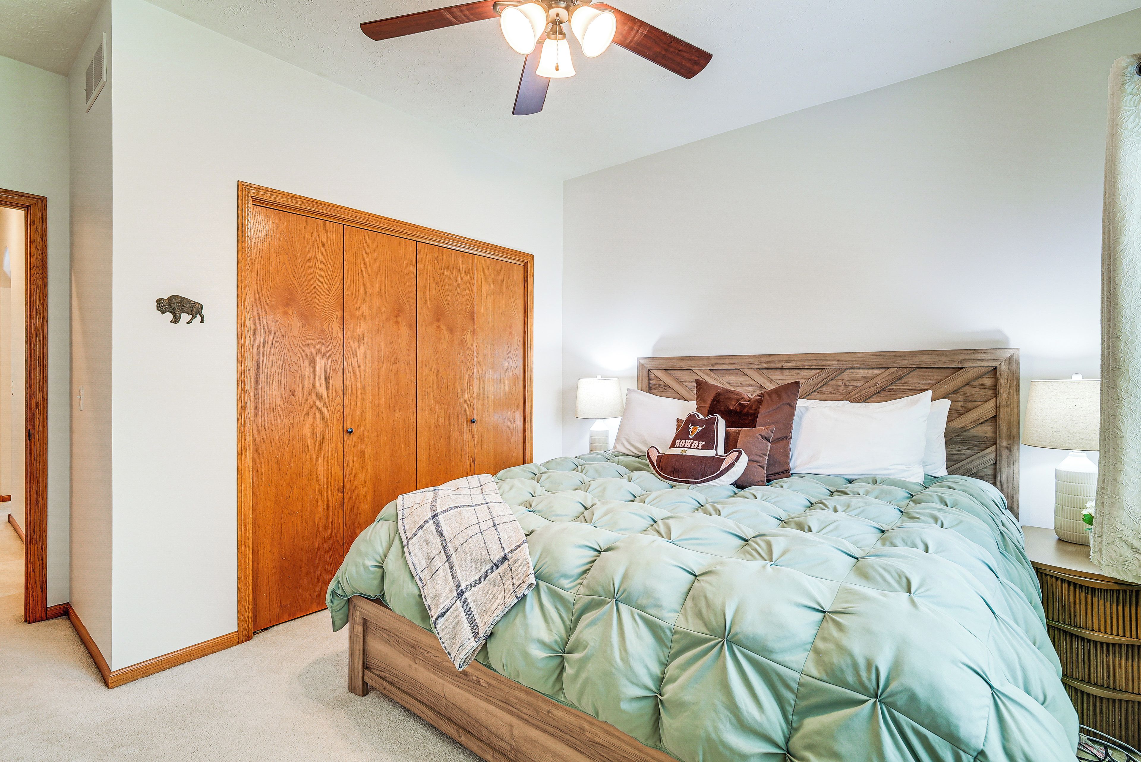 A bedroom with a wooden wardrobe, a bed with a quilted green bedspread, and a ceiling fan.
