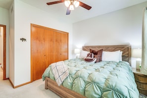 A bedroom with a wooden wardrobe, a bed with a quilted green bedspread, and a ceiling fan.