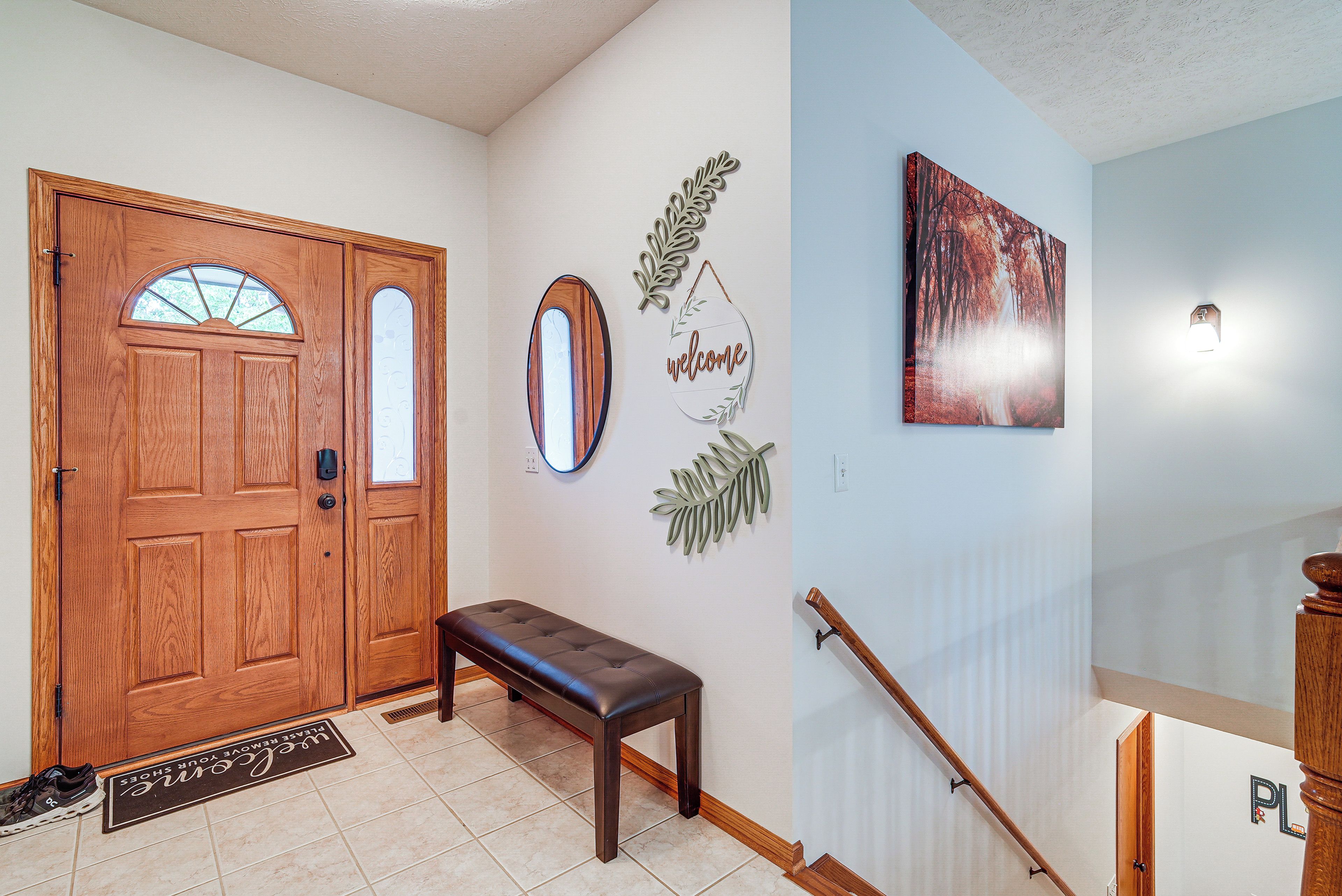 Une porte en bois avec un vitrage, un banc, une pancarte de bienvenue, une décoration en forme de feuille et un tableau accroché au mur.