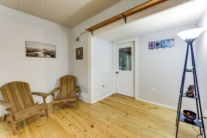 A room with wooden flooring, a wooden chair, a small table, a lamp, and a wall-mounted shelf with a decorative item.