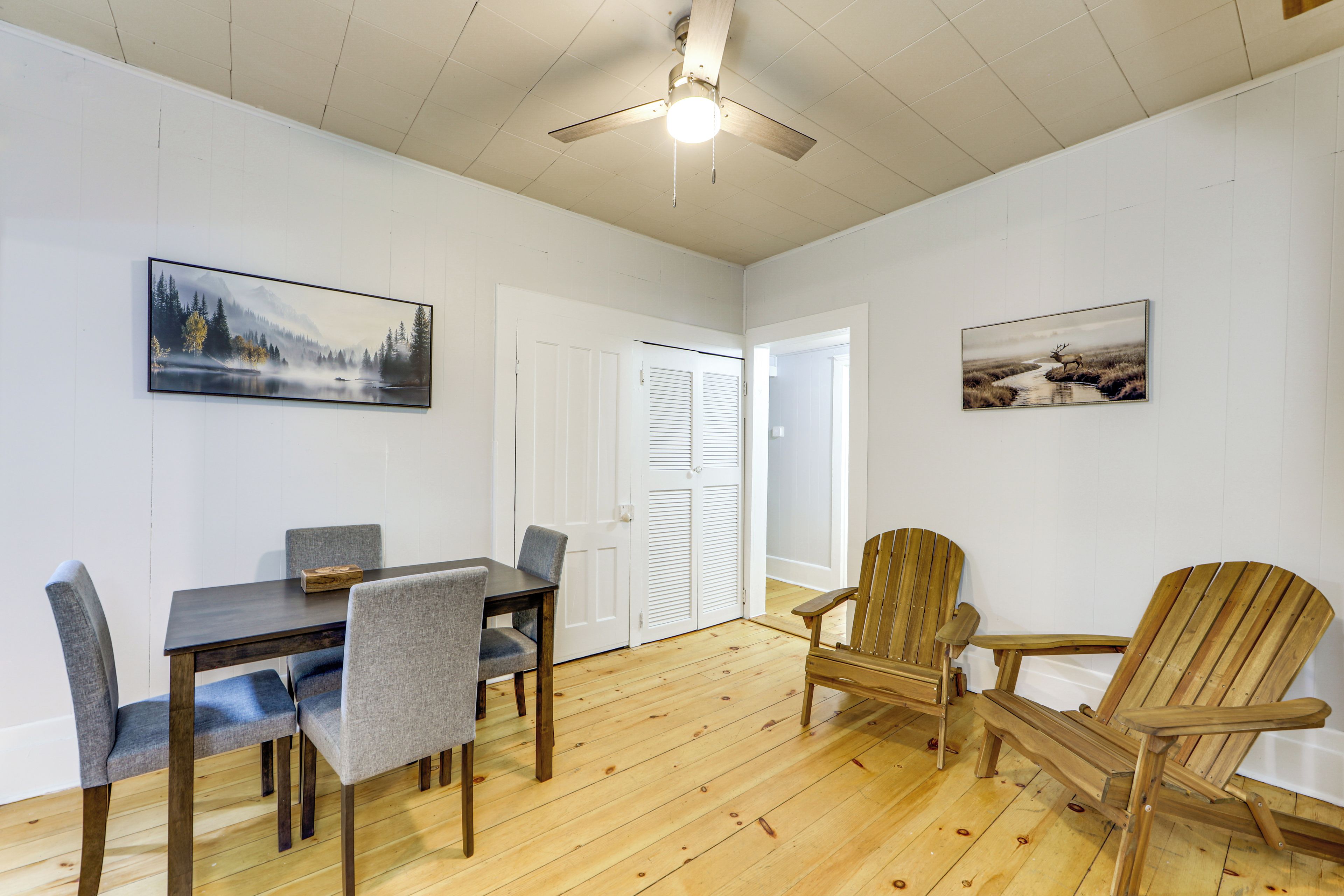A dining area with a table and chairs, a ceiling fan, and two framed pictures on the walls.