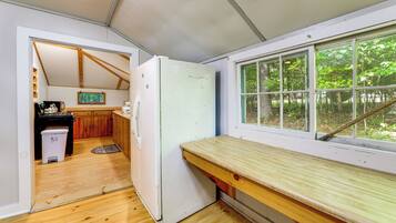A compact kitchen with wooden cabinets, a white refrigerator, and a window overlooking a forest.