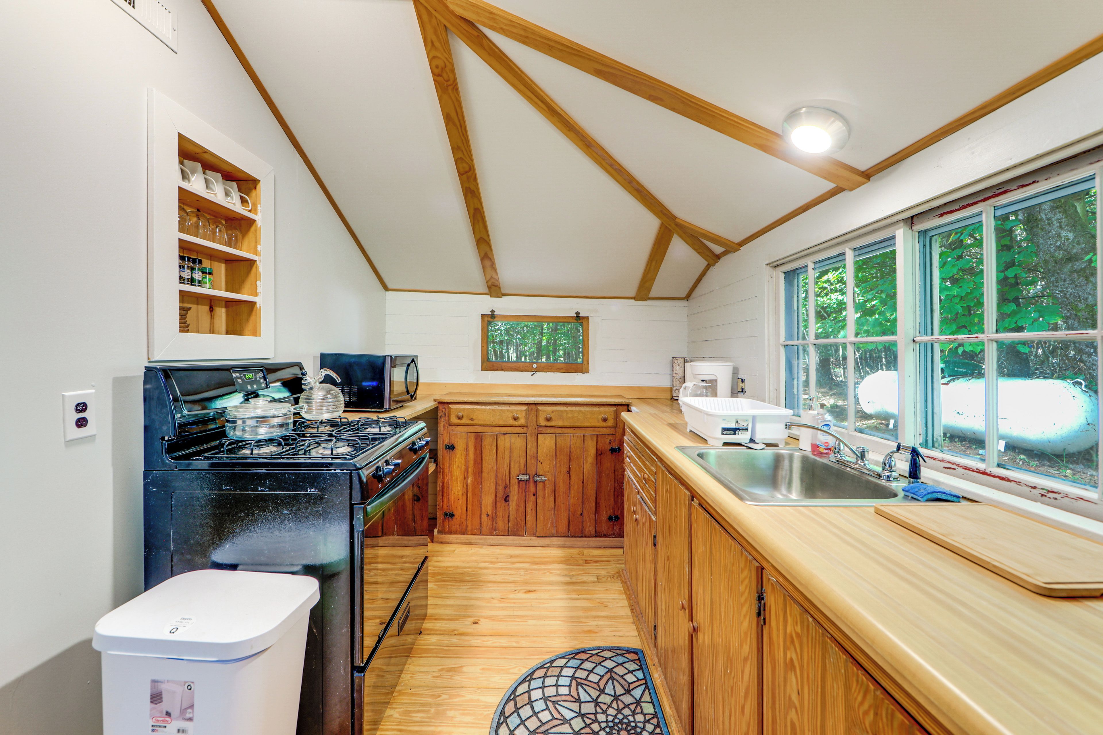 Una cocina con armarios de madera, una estufa y una ventana con vistas a árboles.
