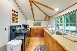 A kitchen with wooden cabinets, a stove, and a window with a view of trees.