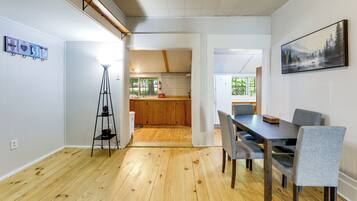 A modern kitchen with wooden cabinets, a dining area with a table and chairs, and a hallway leading to a bedroom.