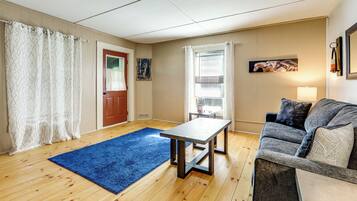 A living room with a blue rug, a wooden floor, a grey sofa, a small table, and a door with a red frame.