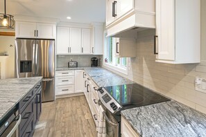 A modern kitchen with white cabinetry, a stainless steel refrigerator, a built-in oven, and a granite countertop. - 13-acre Vermont Estate w/ Hot Tub & Game Room (West Dover)