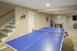 A room with a ping pong table, a staircase, a door, and a wall clock. - 13-acre Vermont Estate w/ Hot Tub & Game Room (West Dover)