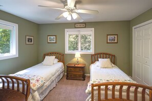 A bedroom with two single beds, a ceiling fan, a window with a view of trees, and a door. - 13-acre Vermont Estate w/ Hot Tub & Game Room (West Dover)