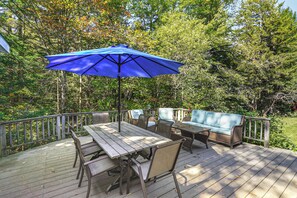 A wooden deck with a table and chairs, a blue umbrella, and a wicker sofa. - 13-acre Vermont Estate w/ Hot Tub & Game Room (West Dover)