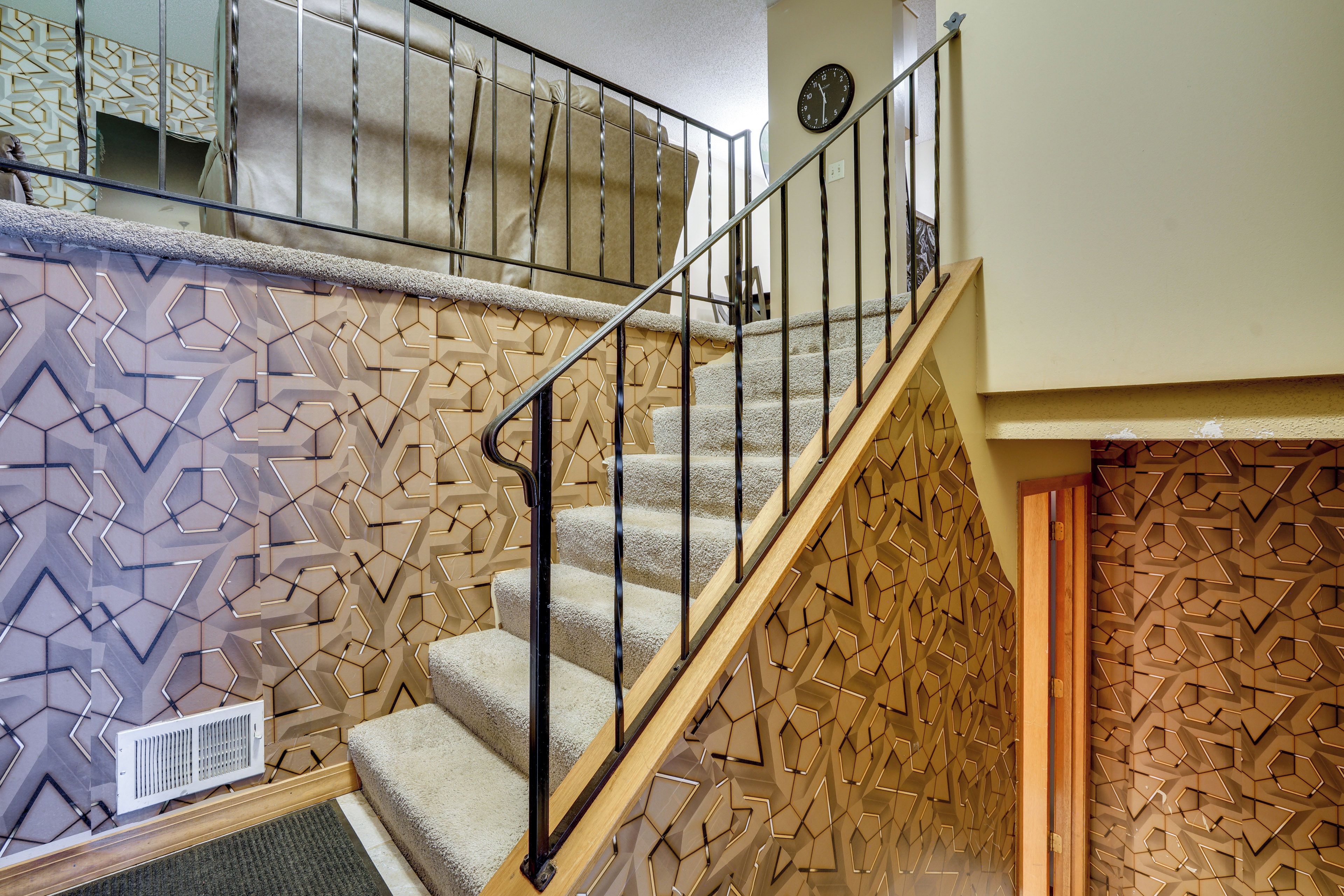 A staircase with geometric patterned walls, a metal handrail, and a carpeted landing.