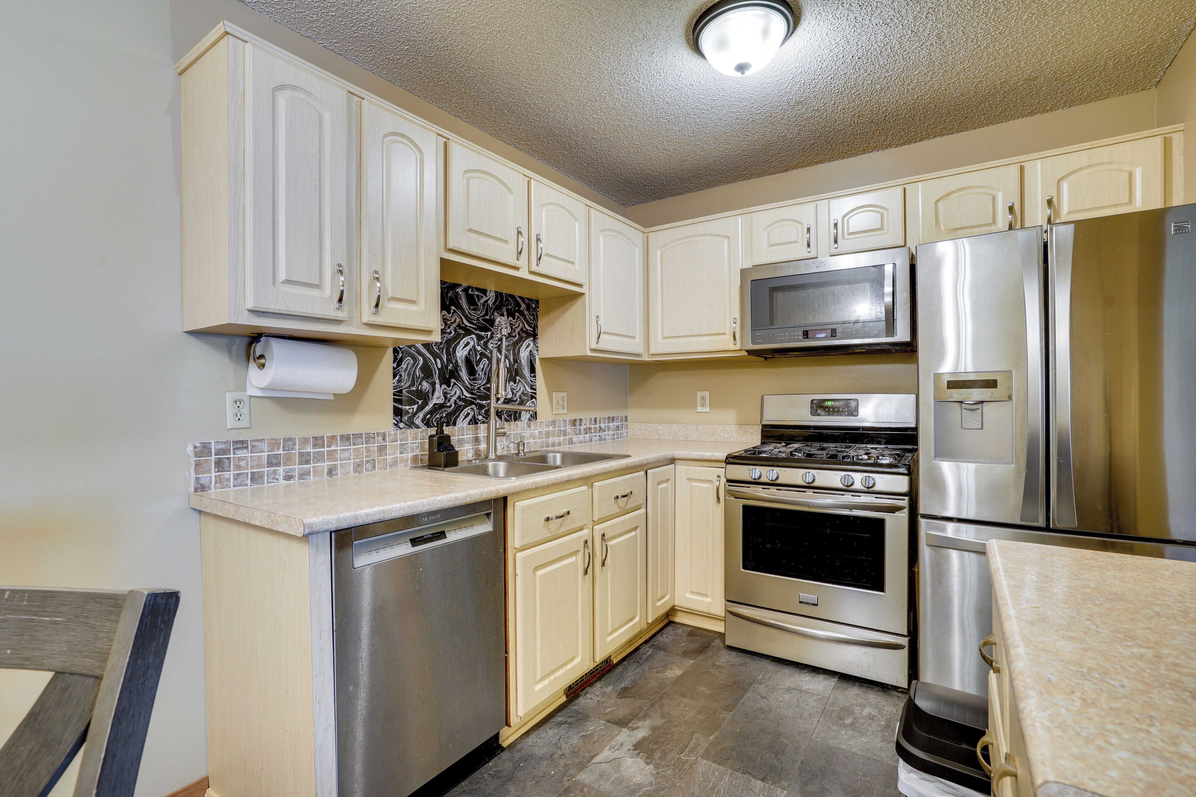 A kitchen with white cabinets, a stainless steel refrigerator, a microwave, a dishwasher, and a tiled backsplash.
