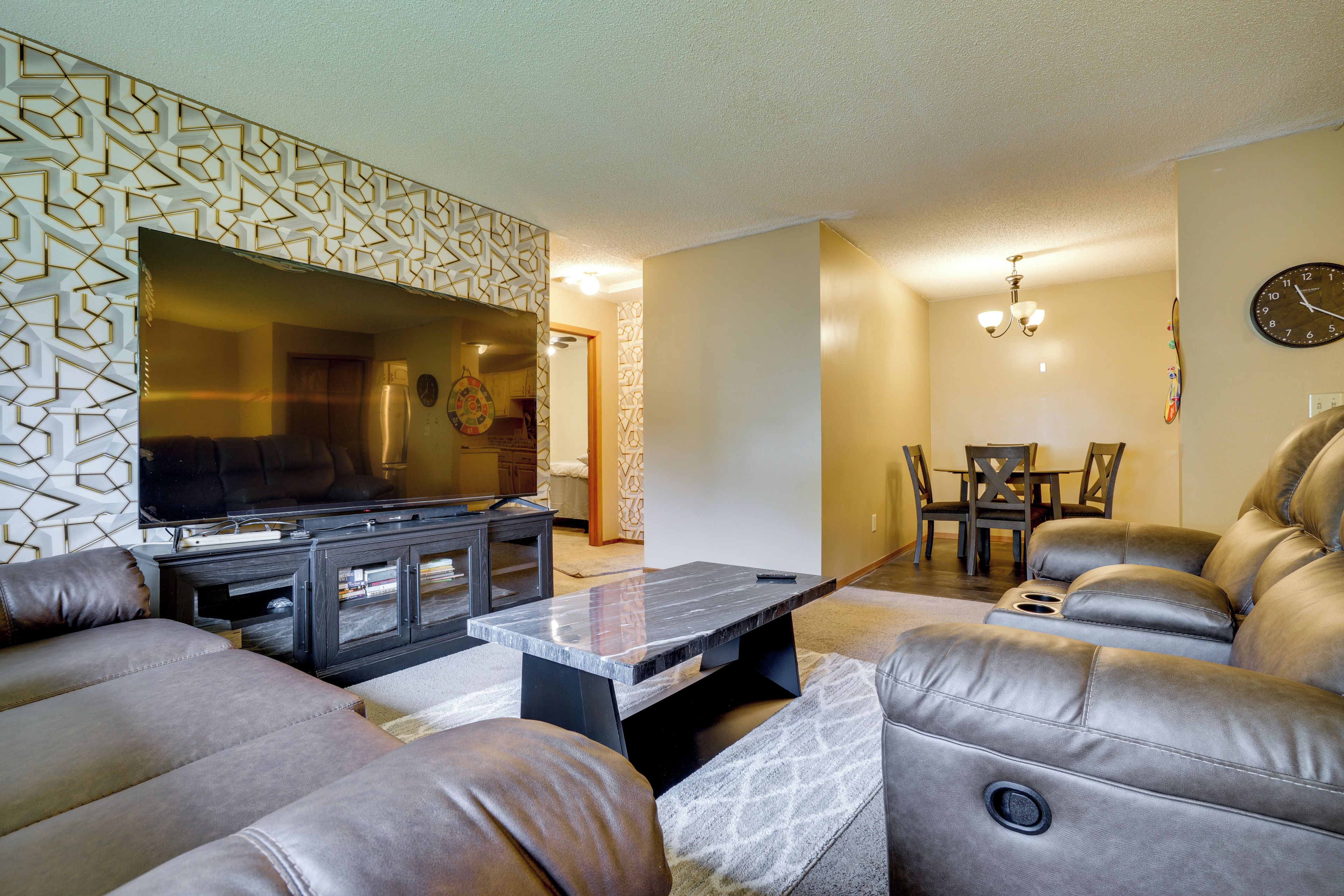 A living room with a flat-screen TV, leather sofas, a coffee table, and a dining area with a chandelier.