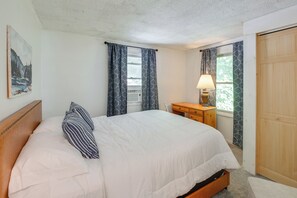 A bedroom with a bed, a bedside table with a lamp, a wooden wardrobe, and a painting on the wall. - Deck & Private Trails! Hancock Forest Hideaway (Hancock)