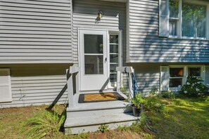 A white house with a front door, a small porch, and a garden area. - Deck & Private Trails! Hancock Forest Hideaway (Hancock)