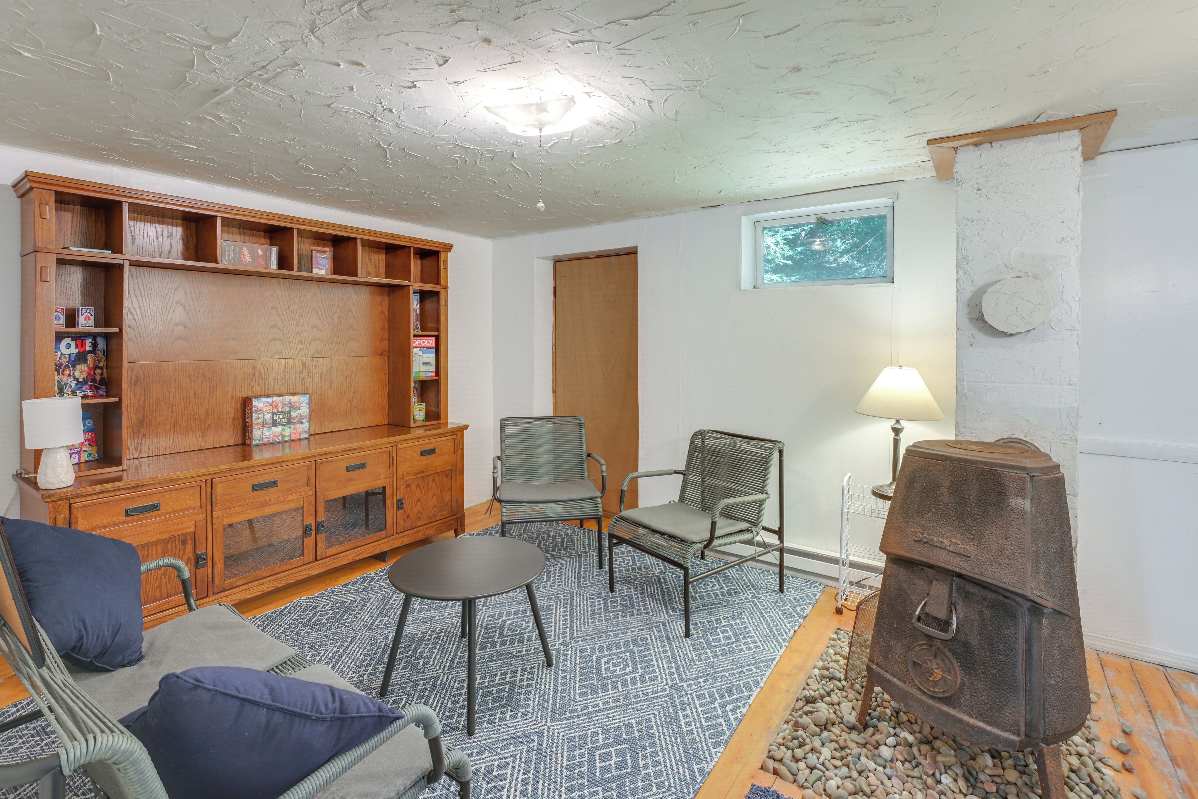 A cozy living room with a wooden entertainment center, two chairs, a small table, a fireplace, and a window.