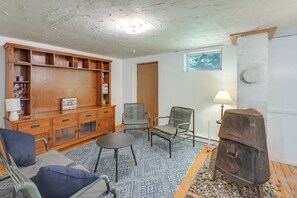 A cozy living room with a wooden entertainment center, two chairs, a small table, a fireplace, and a window. - Deck & Private Trails! Hancock Forest Hideaway (Hancock)