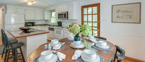 A modern kitchen with white cabinets, a microwave, and a sink. There's a dining table set with plates, cups, and a vase of flowers.