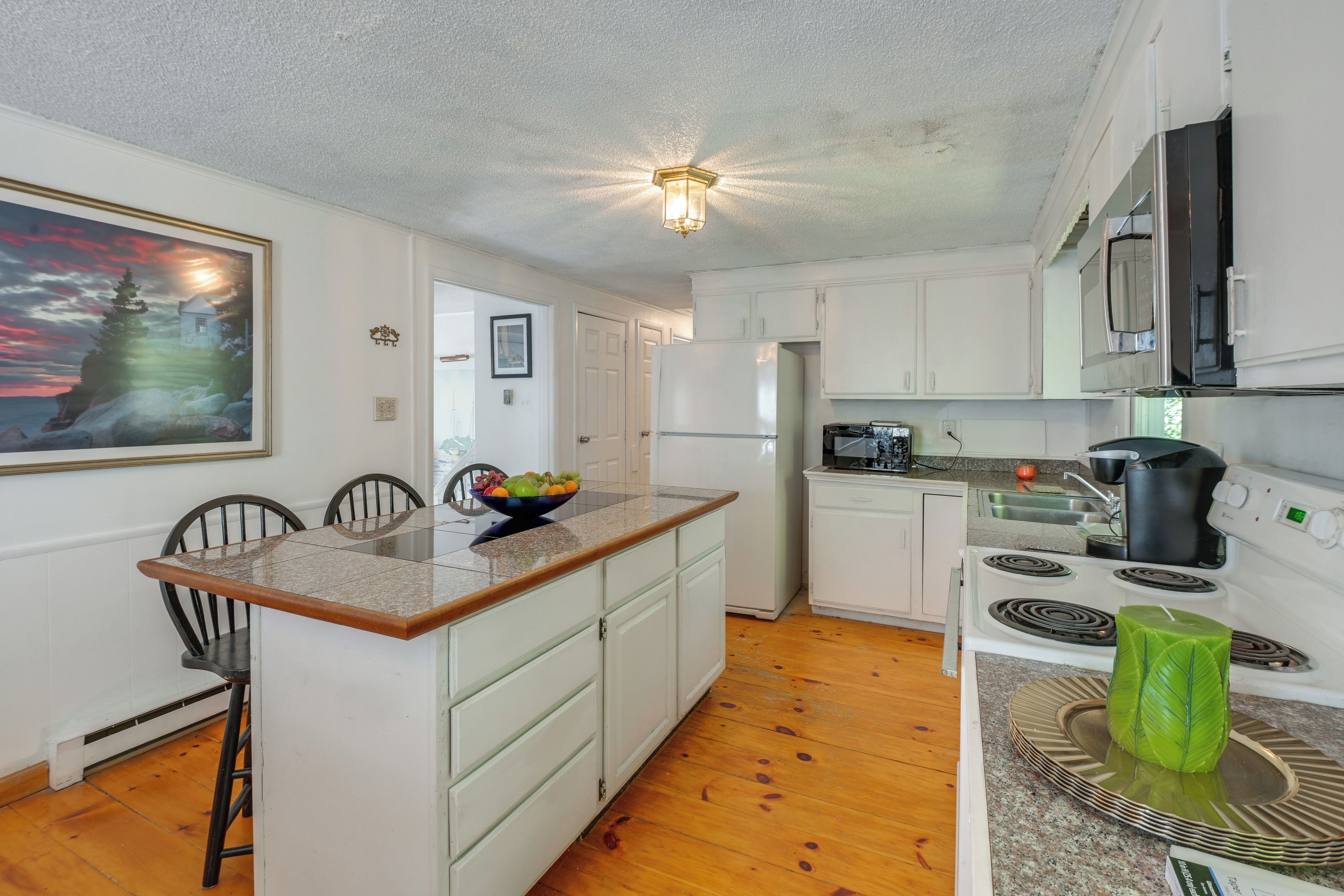 A compact kitchen with white cabinets, a granite countertop, a stove, a microwave, and a refrigerator.