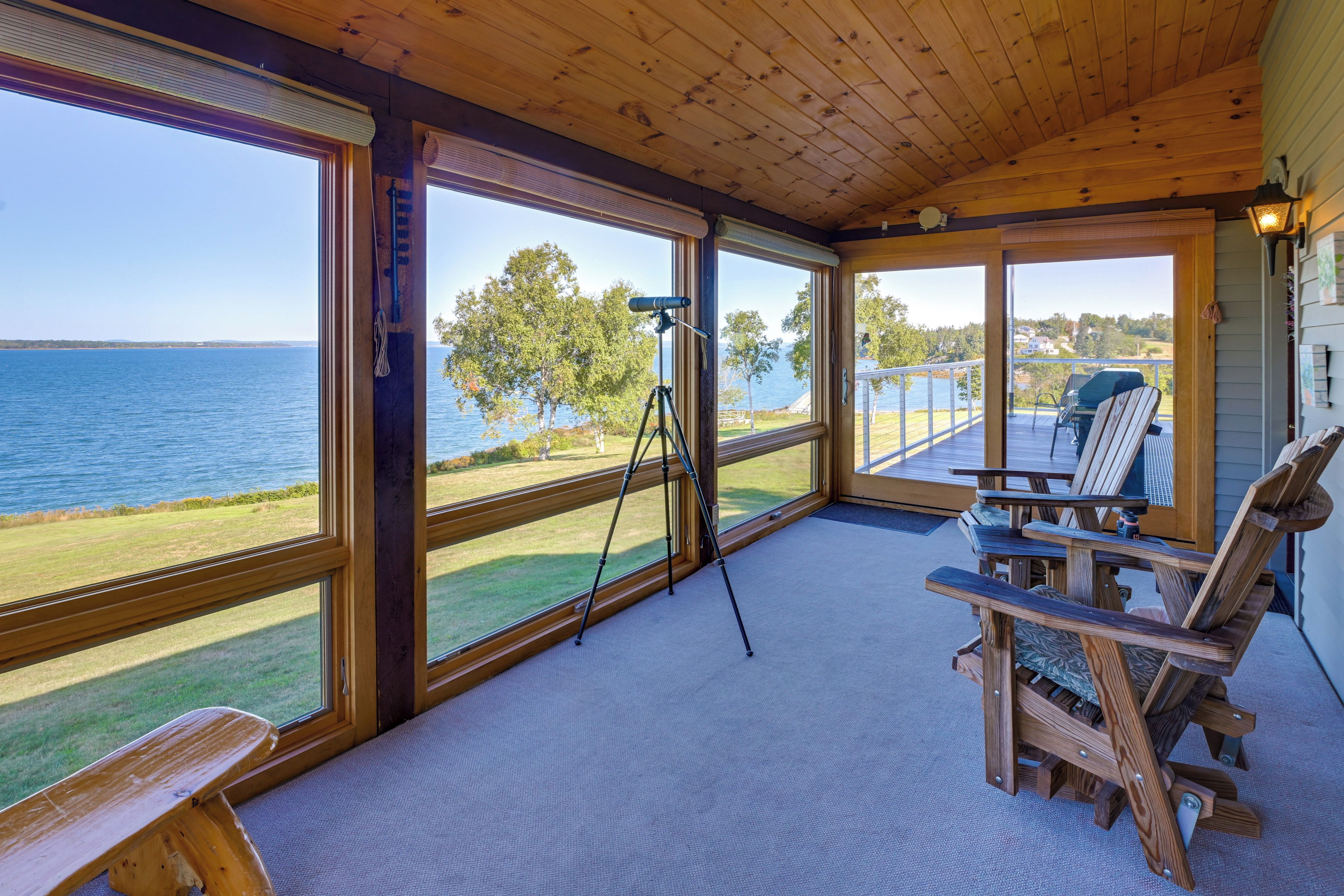 A covered deck with a telescope, wooden chairs, and a view of the water.
