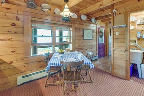 A wooden cabin interior with a dining table set for four, a chandelier, and a large window. - Shorefront Maine Escape! Paddle, Hike & Stargaze (Harborside)