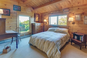 A wooden cabin bedroom with a bed, dresser, desk, and chair.