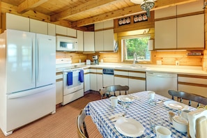 A compact kitchen with a refrigerator, microwave, stove, and sink. There's a dining table set with plates, glasses, and cutlery. - Shorefront Maine Escape! Paddle, Hike & Stargaze (Harborside)