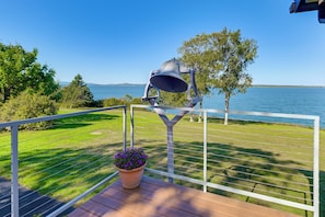 A balcony with a view of a lake, a metal bell, and a potted plant.