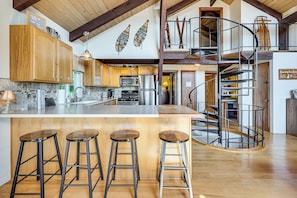 A spacious kitchen with modern appliances, a large island with stools, and a spiral staircase. - White Mtn Views & Game Room in Edelweiss Village (Madison)