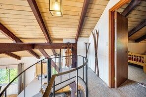 A wooden interior with a spiral staircase, wooden beams, and a view of the outdoors. - White Mtn Views & Game Room in Edelweiss Village (Madison)